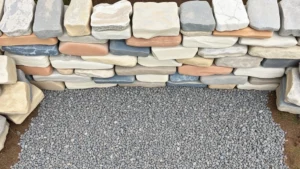 Overhead view of carefully stacked natural stone garden wall foundation with compacted gravel base, showing proper stone placement and interlocking pattern for stability