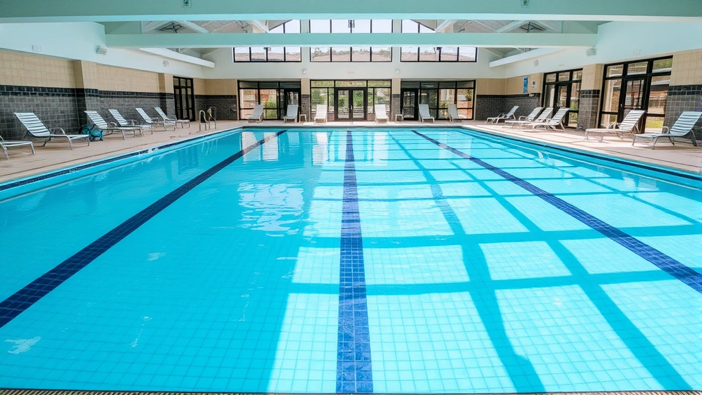 Bright indoor heated swimming pool with clear blue water, surrounded by comfortable lounge chairs and modern architectural design. Family-friendly aquatic facility with professional maintenance and contemporary tile work.