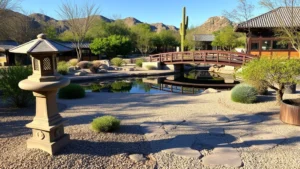 Serene Japanese garden with stone lantern, carefully raked gravel pathways, lush green plants, and traditional wooden bridge over calm reflecting pond, Phoenix desert setting in background, morning light creating soft shadows